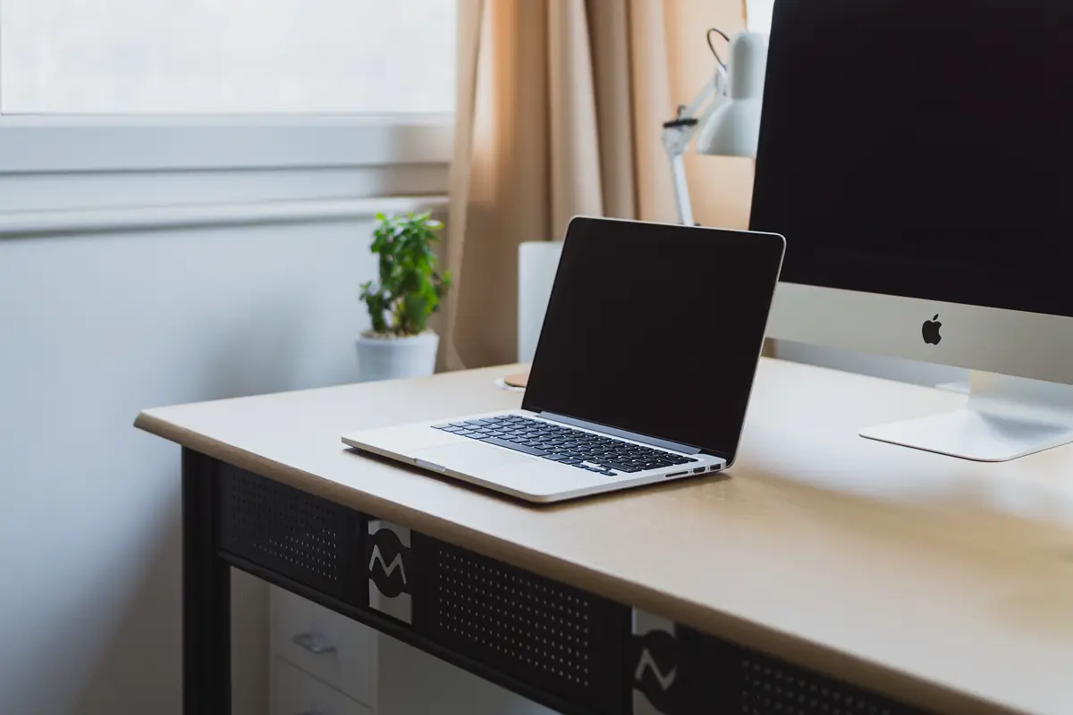 A laptop open on a wooden desk beside a desktop monitor, a typical setup for researching a domain name.