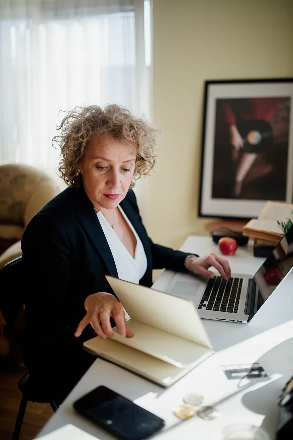 A person working at a bright desk with a laptop, an open notebook and a phone.