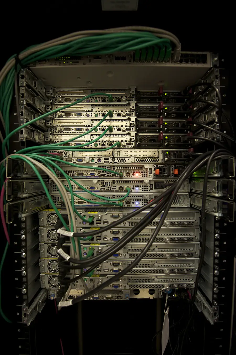 A server rack with stacked machines and bundles of green, black and grey network cables.